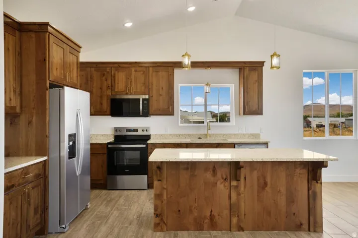 Kitchen featuring wood-finish cabinetry, stainless steel appliances, light-toned countertops, a spacious island with a matching countertop, and vaulted ceilings