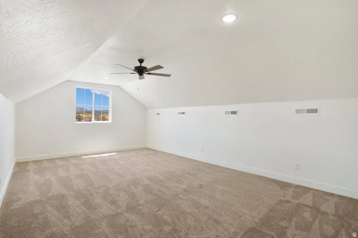 Spacious room featuring vaulted ceilings, a prominent window, beige carpet flooring, and a ceiling fan
