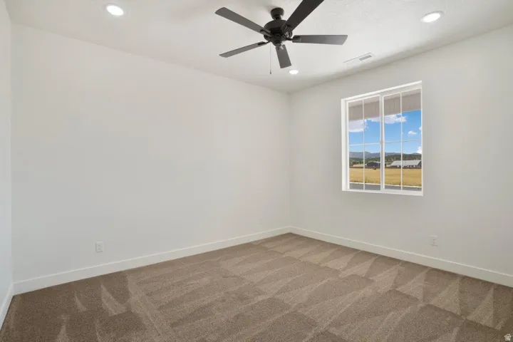 Spacious room featuring neutral carpet, white walls, and a modern ceiling fan with integrated lighting