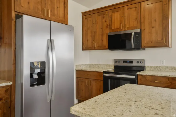 Kitchen featuring wood cabinetry, light-toned stone countertops, stainless steel side-by-side refrigerator, built-in microwave, and electric range