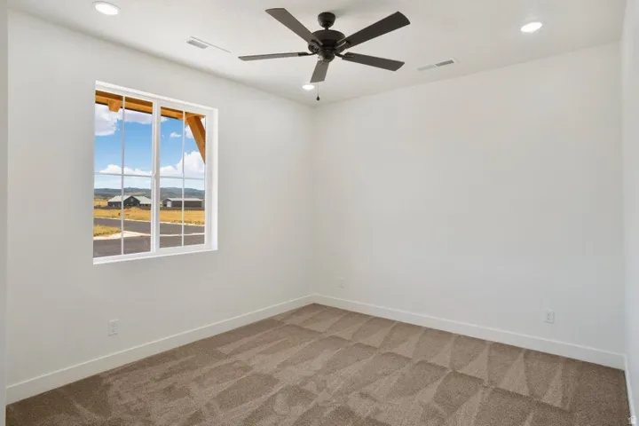 Bright room featuring a large multi-pane window, flush-mounted ceiling lighting, a dark-toned ceiling fan, light-colored walls, and textured carpeting