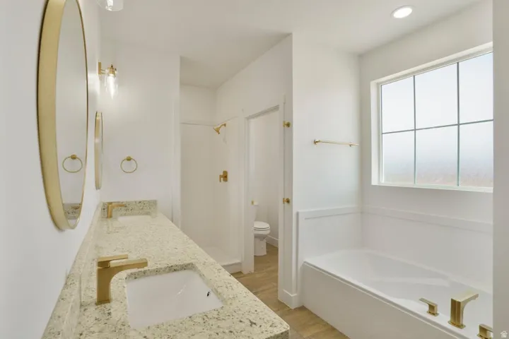 Modern bathroom featuring a double vanity with granite countertops, gold-finish fixtures, and oval mirrors
