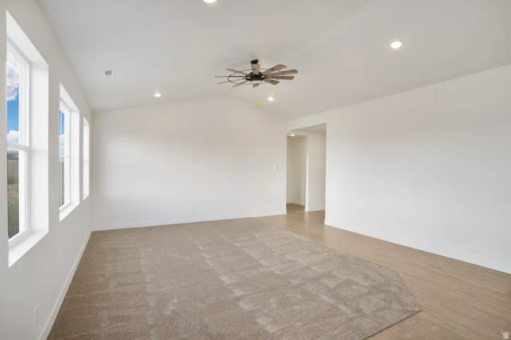 Spacious living area featuring a vaulted ceiling with a ceiling fan, recessed lighting, and multiple windows providing natural light