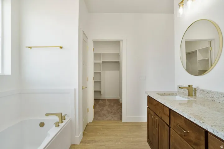 Bathroom featuring a freestanding tub with gold-finish fixtures, a wood-finish vanity with a speckled countertop, and a circular gold-framed mirror