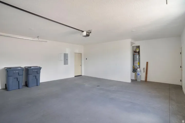Spacious garage with light gray concrete flooring, white painted walls, and a visible water heater installation