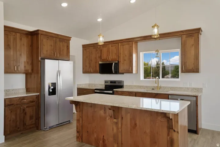 Kitchen featuring extensive wood cabinetry, light-toned granite countertops, stainless steel appliances, and a central island