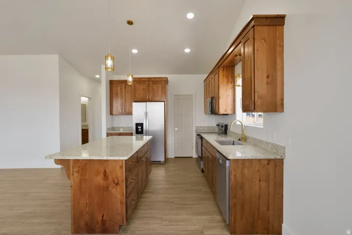 Open-concept kitchen featuring wood-finish cabinetry, light-toned countertops, stainless steel appliances, and wood-finish tile flooring