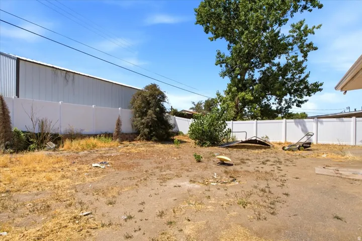Spacious outdoor area featuring a white privacy fence and a mature tree