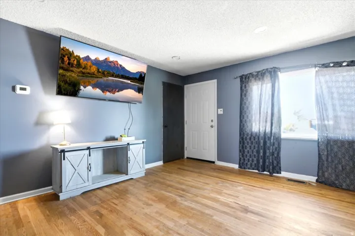 Hardwood flooring throughout featuring a neutral gray wall color, white baseboards, and a white paneled door