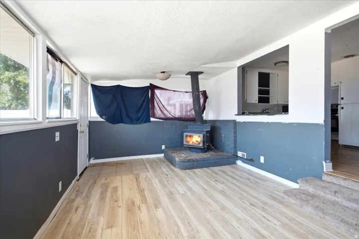 Living area featuring wood-finish flooring, a freestanding wood-burning stove with a brick base, and multiple windows