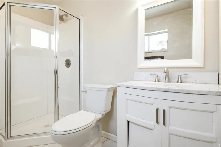 Bathroom featuring a glass-enclosed shower, white vanity with a light-toned countertop, brushed nickel fixtures, and a framed mirror
