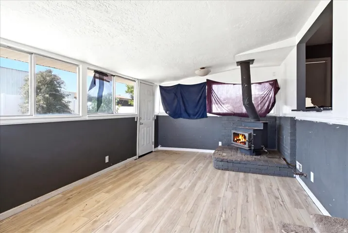 Living area featuring wood-finish flooring, a brick hearth, and a wood-burning stove