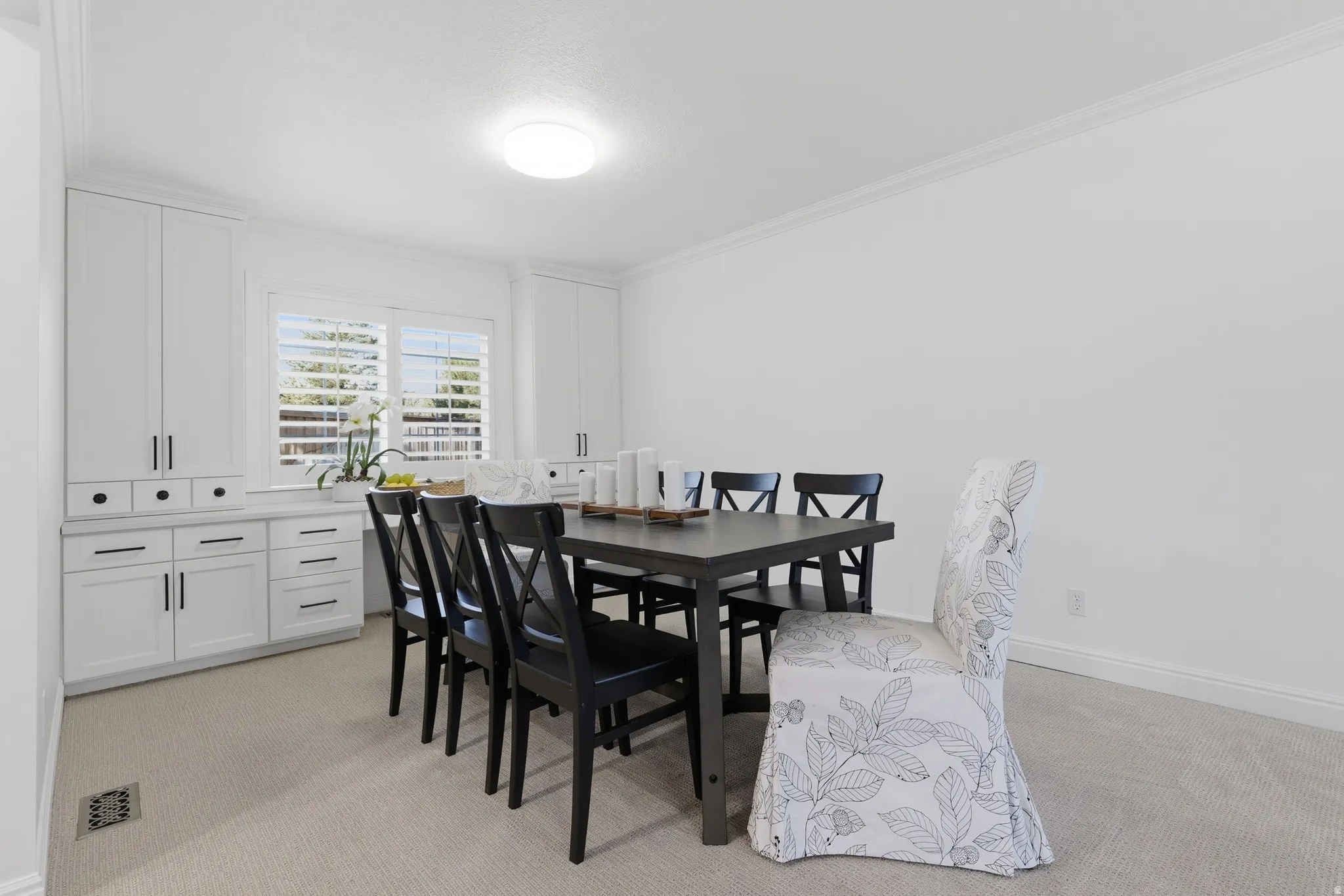Dining or office area featuring built-in cabinetry, a window with plantation shutters, crown molding, a flush-mount ceiling light, and neutral carpeting