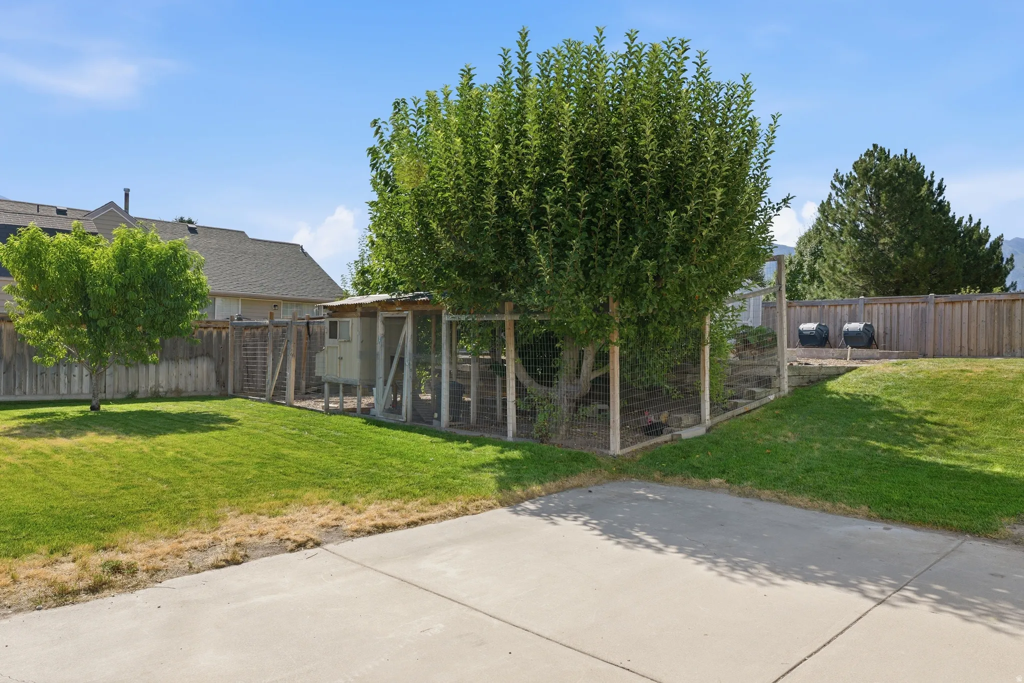 Expansive backyard featuring a chicken coop structure, mature trees, a concrete patio area/ RV parking, and wood fencing