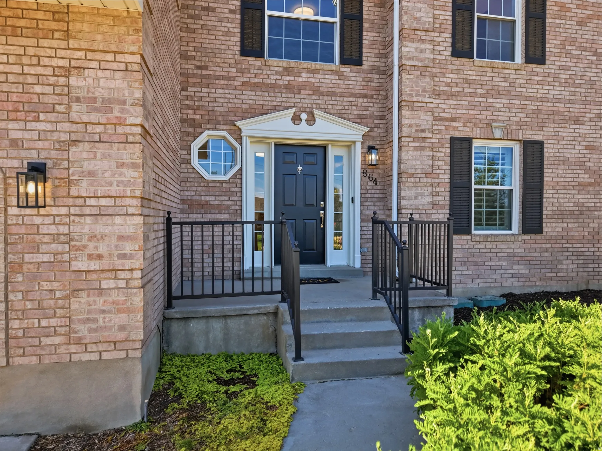 Brick exterior featuring a black entry door with transom window, decorative octagonal window, and black shutters