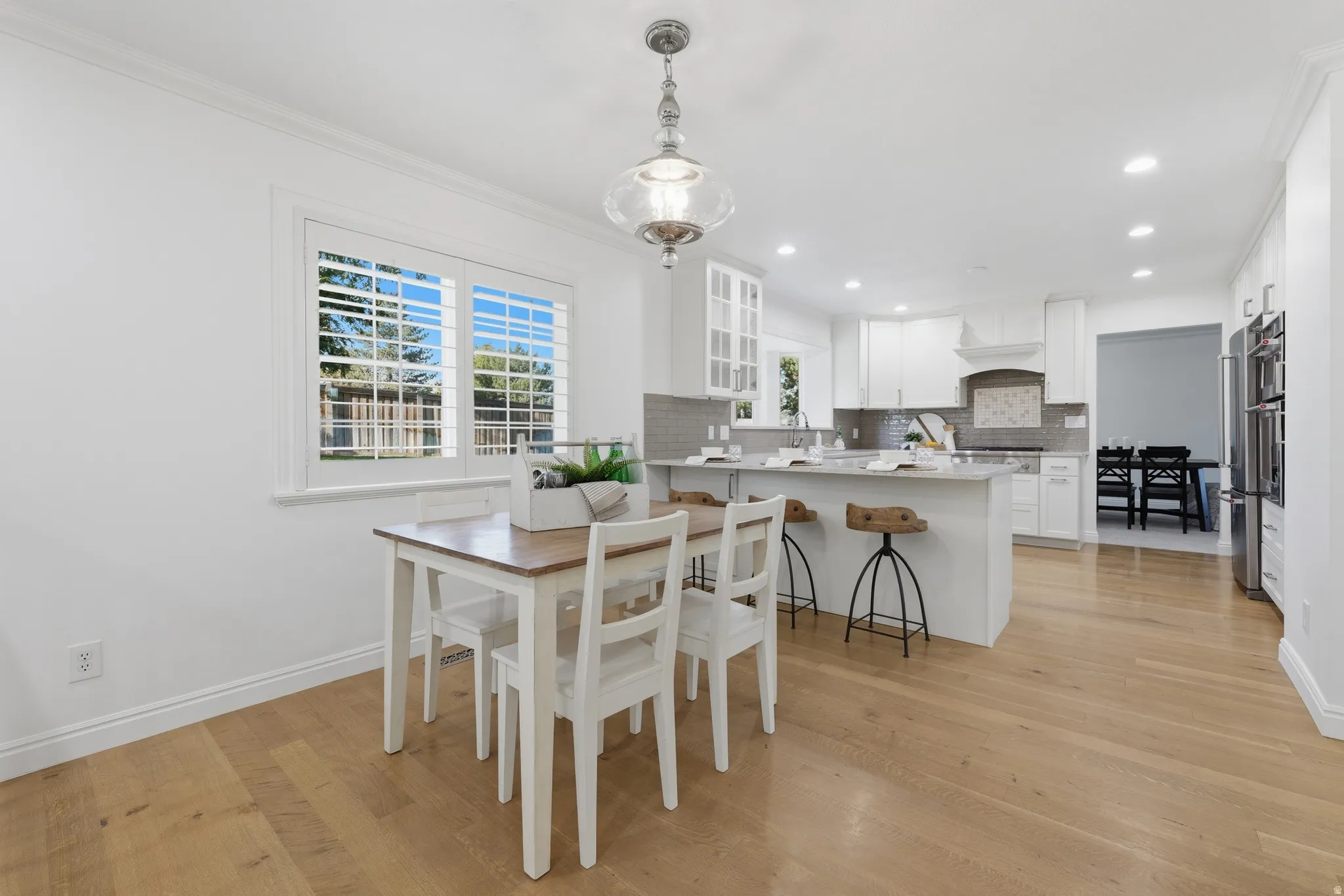 Open-concept kitchen and dining area featuring light hardwood flooring, white cabinetry, a large breakfast area, a subway tile backsplash, and recessed lighting