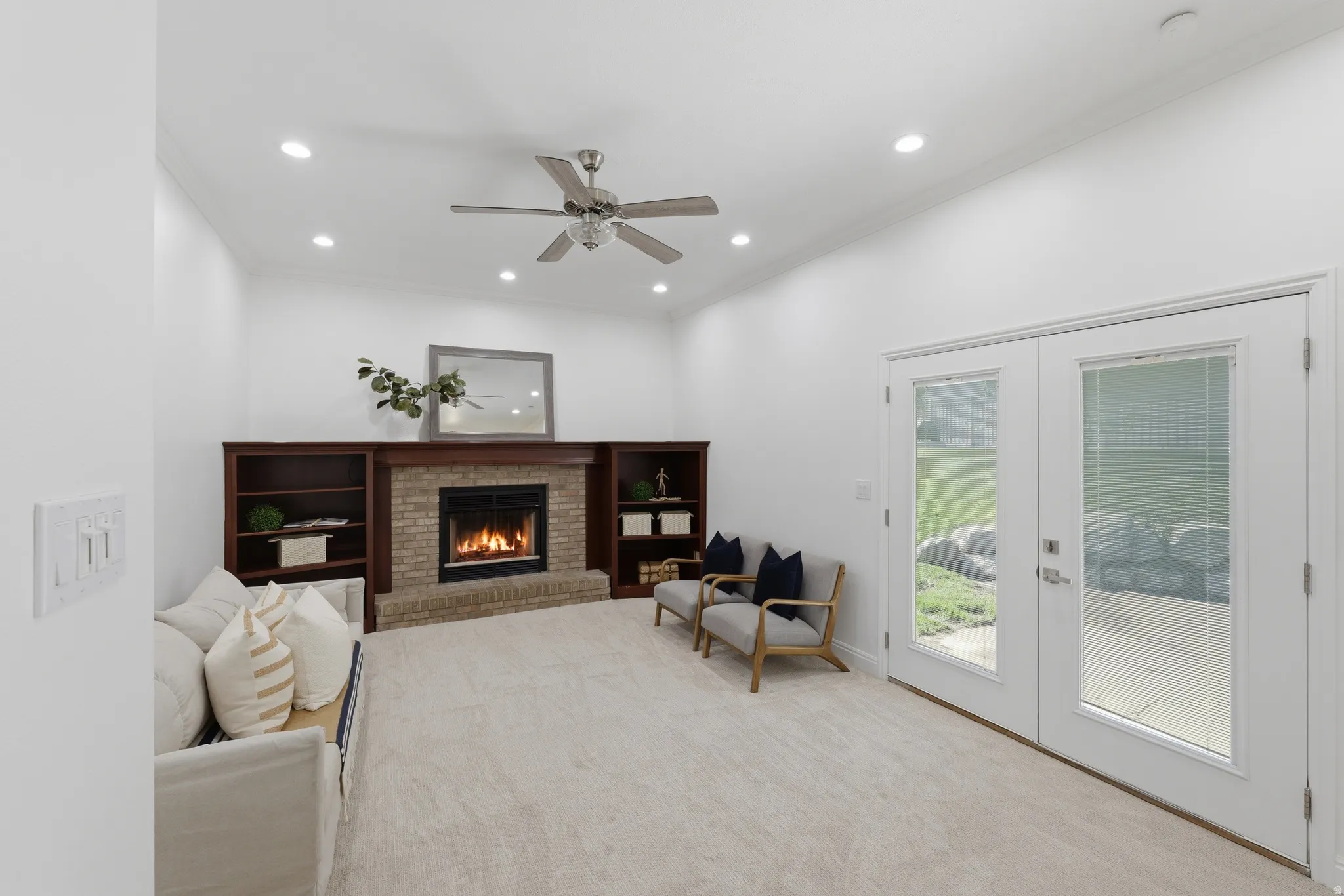 Living room featuring a brick fireplace with a wood mantle, built-in shelving, a ceiling fan, recessed lighting, and double glass-paneled doors leading to backyard