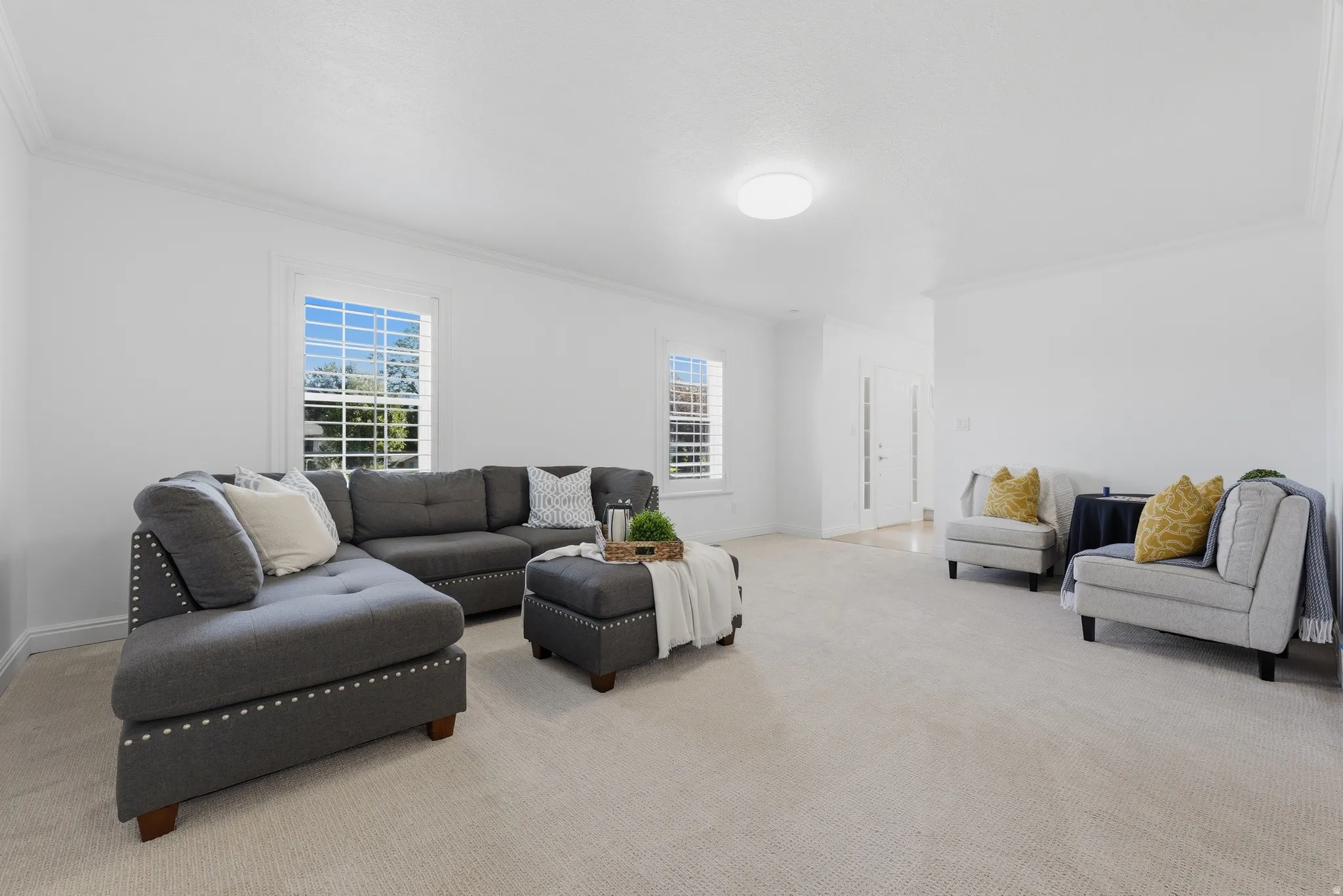 Spacious living area featuring light-toned carpet flooring, white walls, and crown molding