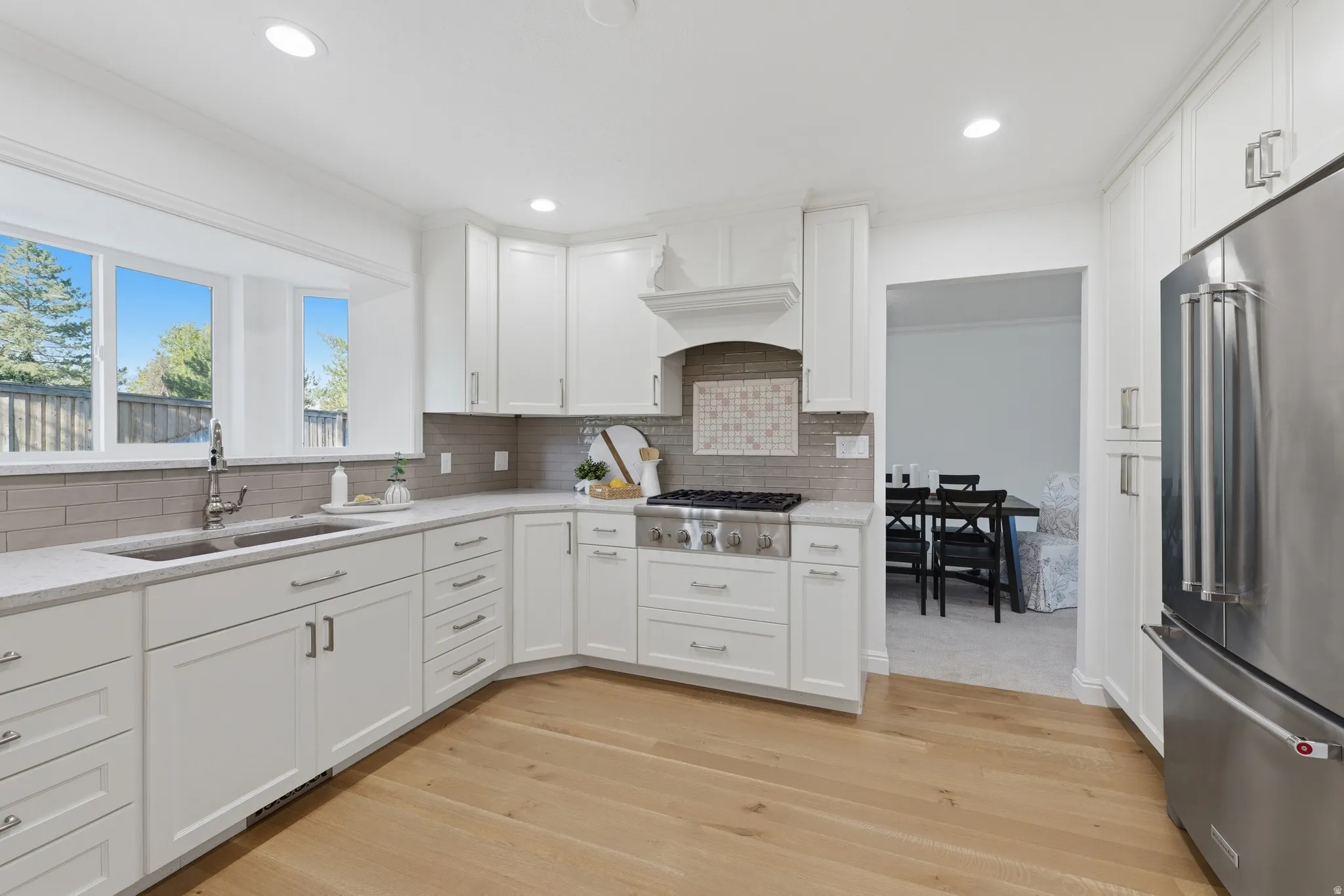 Modern kitchen featuring white cabinetry, light hardwood flooring, recessed lighting, stainless steel appliances, and a bay window