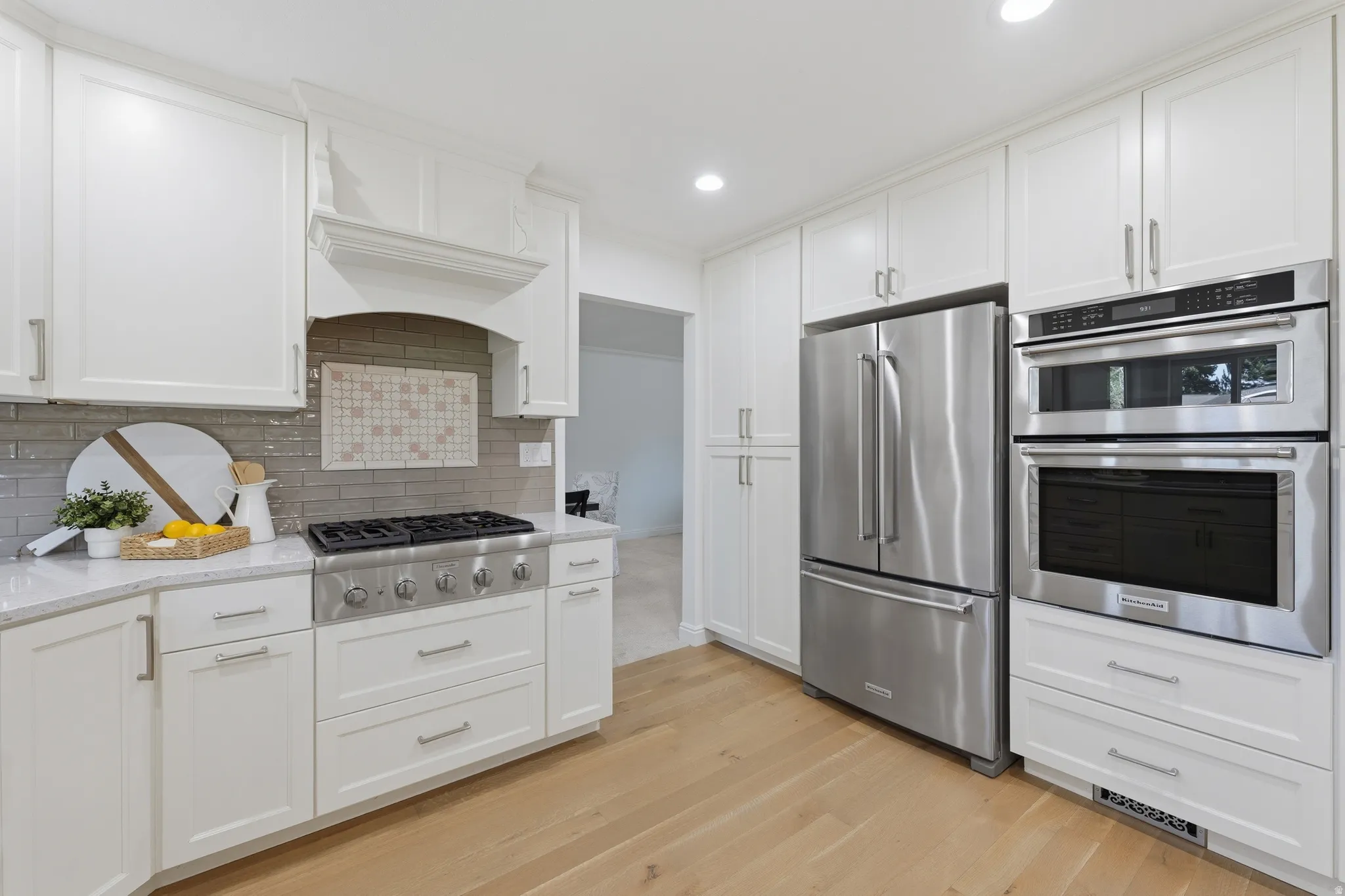 Kitchen featuring white shaker cabinetry, stainless steel appliances, wall oven and countertop gas stove, light hardwood flooring, and a subway tile backsplash