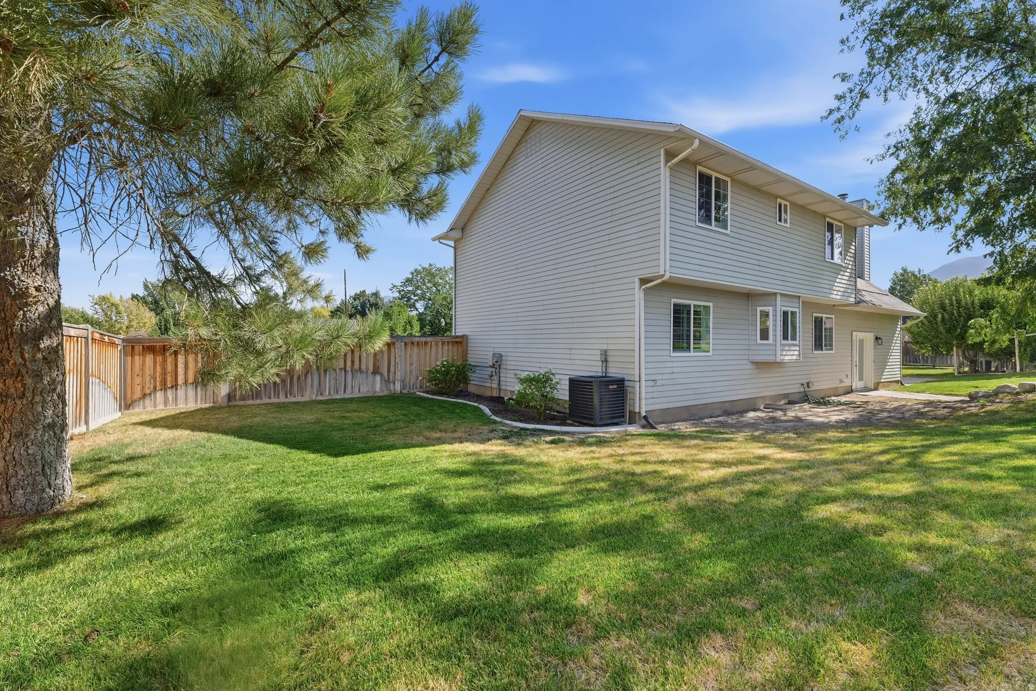 Expansive backyard featuring a manicured lawn, full privacy fencing, established trees, and a concrete patio space