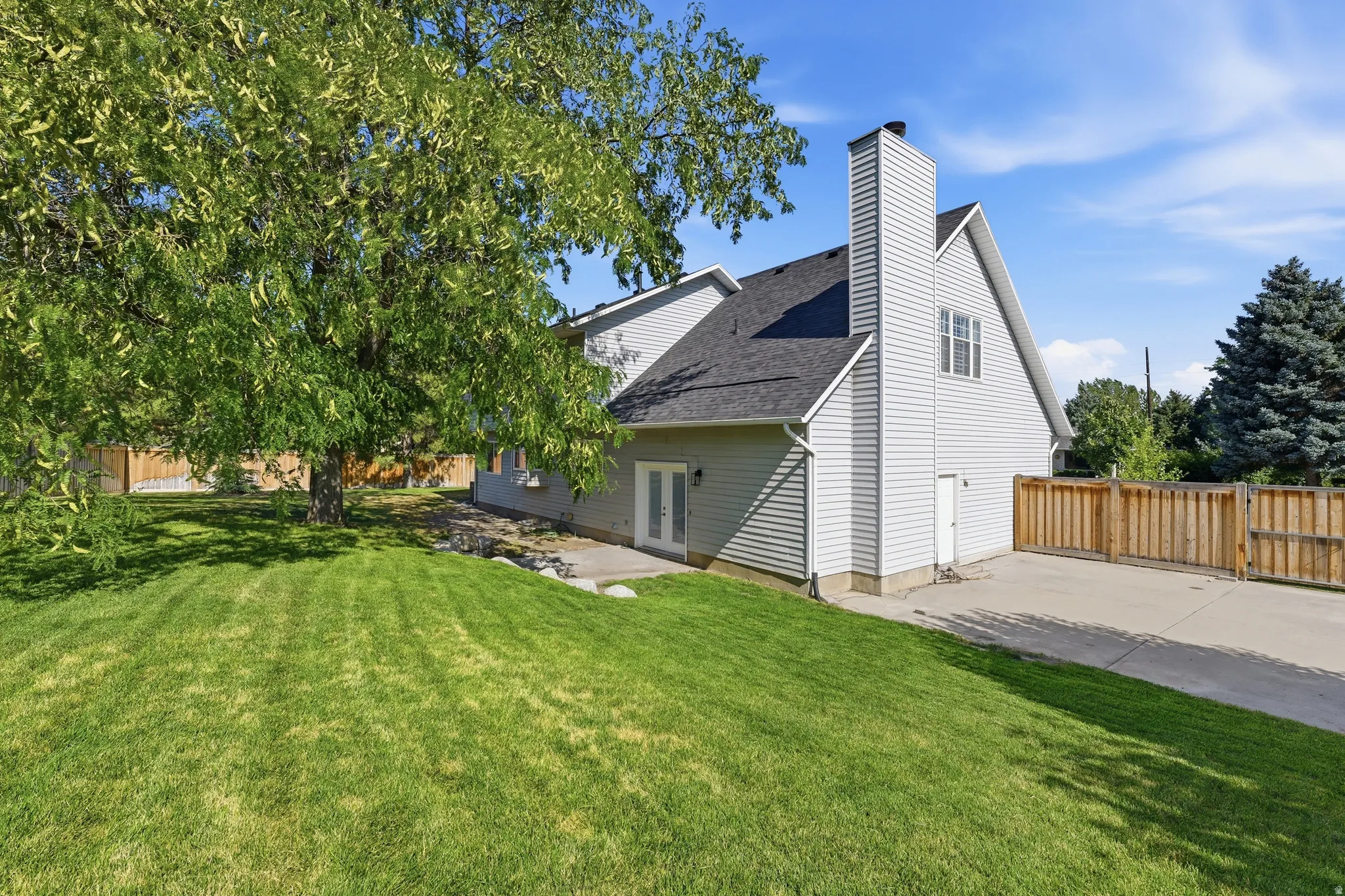 Expansive yard featuring a large mature tree providing natural shade, a healthy lawn, a concrete patio/RV parking area, and a solid wood privacy fence. Gate opening is 10'