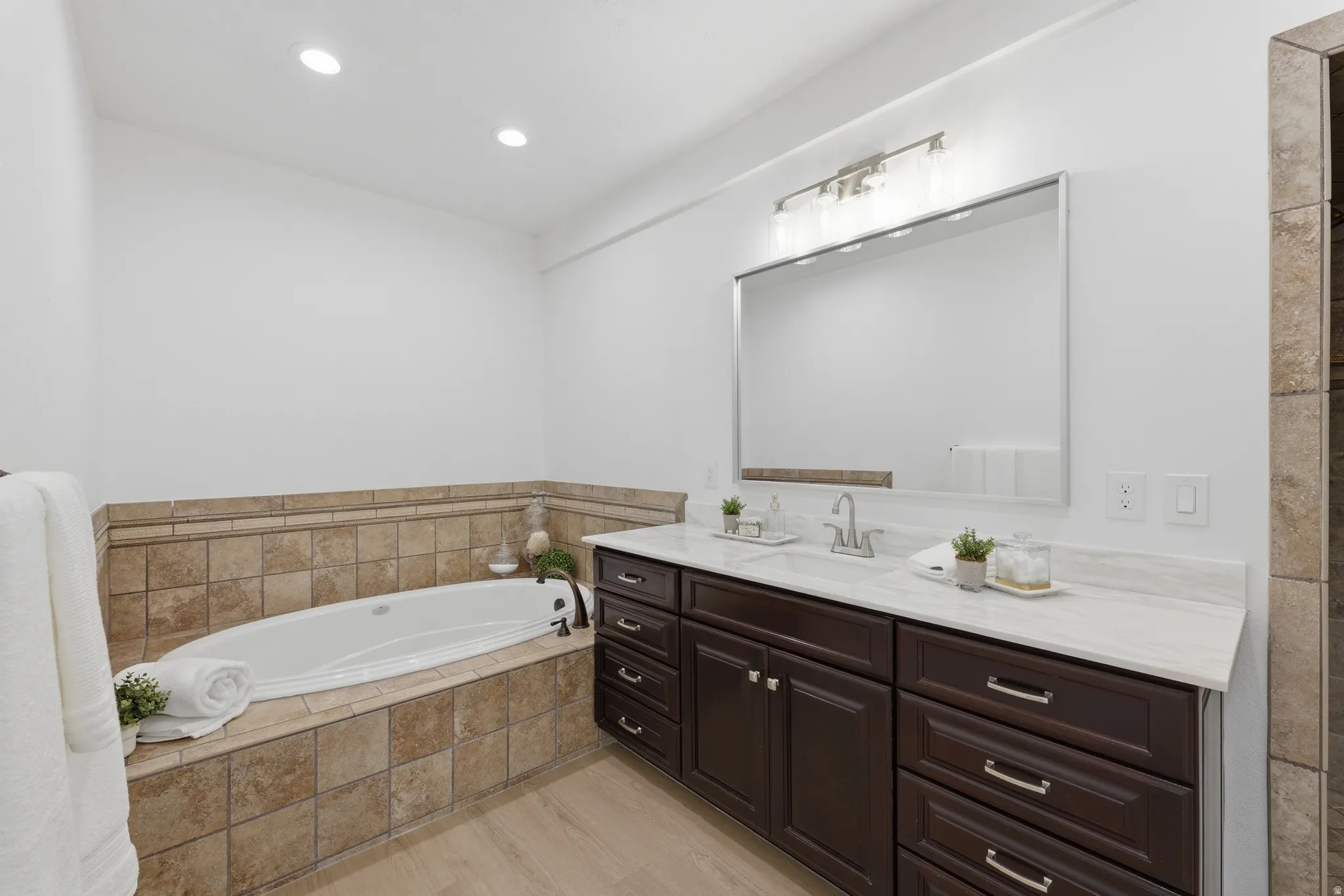Primary bathroom featuring a built-in soaking tub with air bubbles, a dual vanity with a white quartzite countertop, and wood-finish LVP flooring