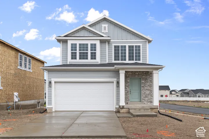 Two-story exterior featuring light gray horizontal and vertical siding, stacked stone accents, a covered front entryway with square columns, and a double-wide concrete driveway