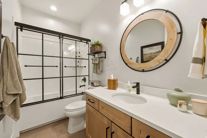 Bathroom featuring a wood-finish vanity with a light-colored countertop, a single undermount sink, and a black-framed shower with sliding glass doors