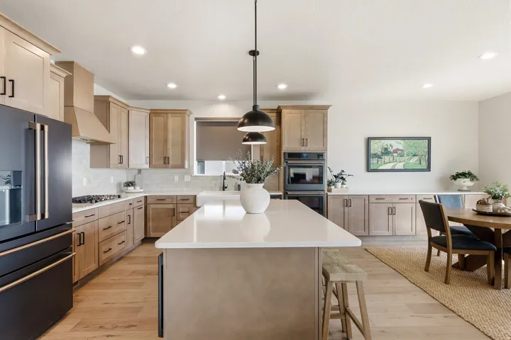 Kitchen featuring light wood-finish cabinetry, white countertops, built-in double ovens, and a central island with pendant lighting