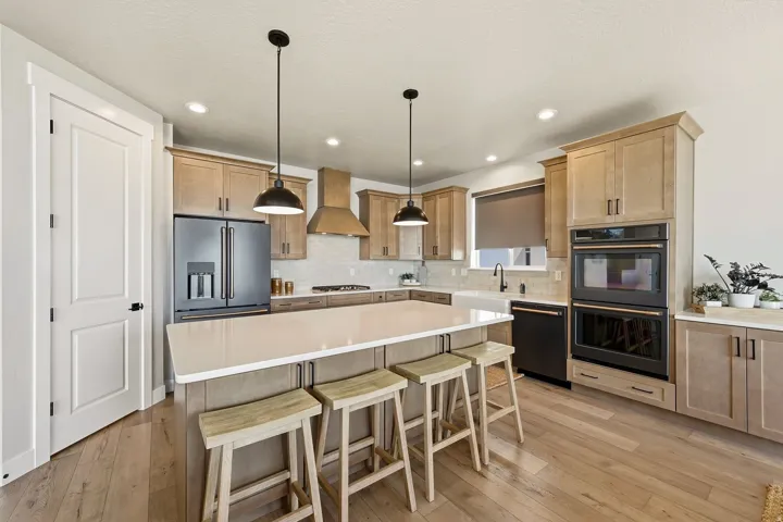 Kitchen featuring wood-finish flooring, light wood cabinetry, a center island with a light-toned countertop, black-finish appliances, and recessed lighting