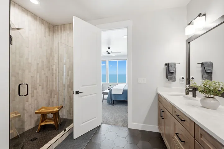 Spacious bathroom featuring a glass-enclosed shower with tile surround, a large vanity with ample storage, a wide mirror, and hexagonal floor tiling