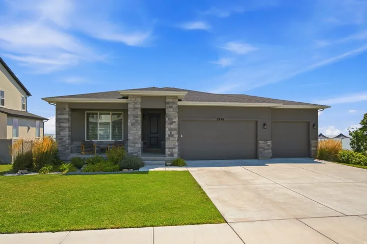 Contemporary stucco and stone exterior with a covered porch, a two-car garage, and a concrete driveway
