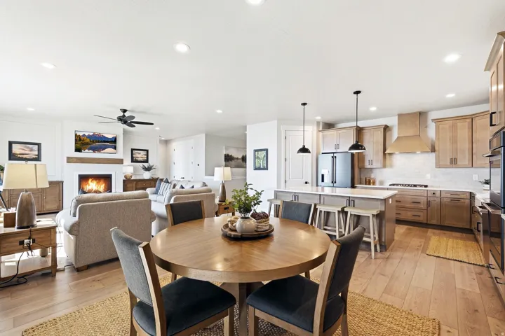 Open-concept living area with wood-finish flooring, a kitchen island with pendant lighting, a fireplace with a wood mantle, and recessed lighting