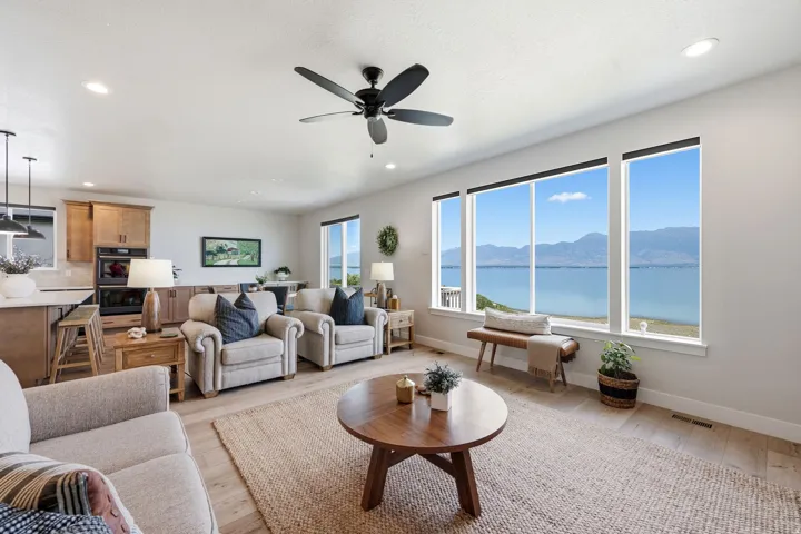 Expansive living area with large windows, light wood-finish flooring, a ceiling fan, recessed lighting, and an open-concept kitchen featuring wood cabinetry and an island with pendant lighting