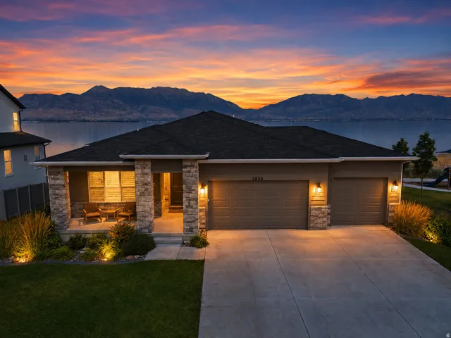 Stone facade accents, covered front porch, attached double garage, concrete driveway, and landscaped front yard