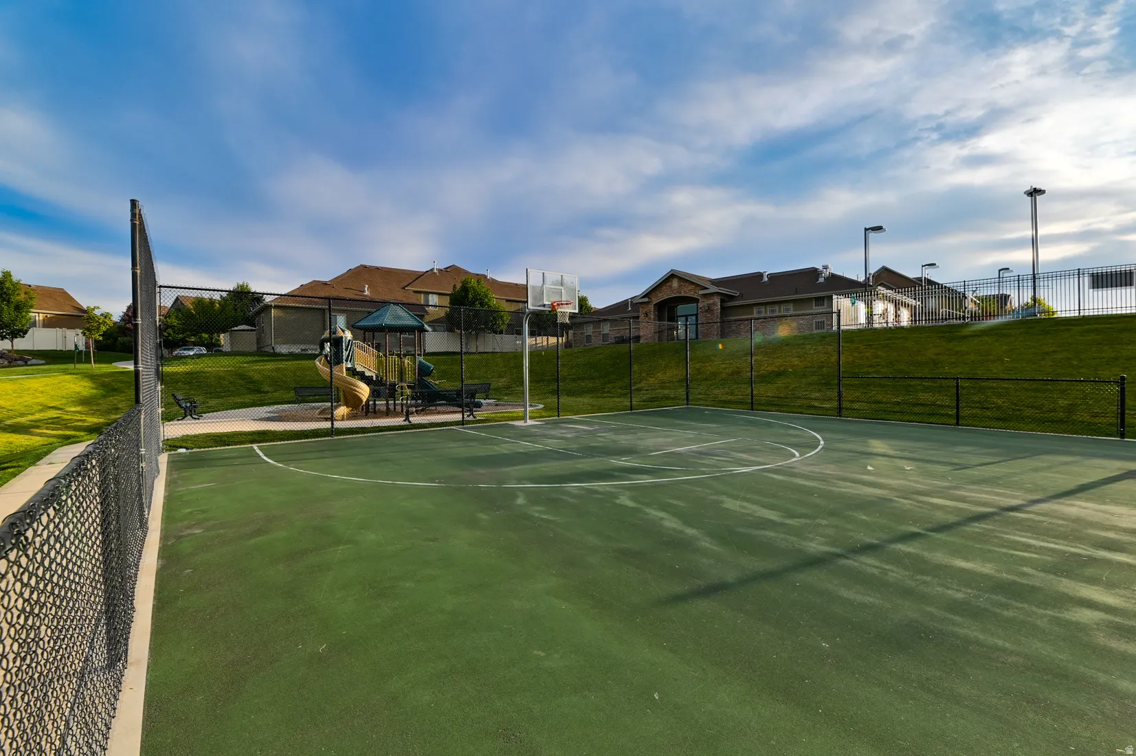 Green-surfaced sports court with a basketball hoop, surrounded by a chain-link fence