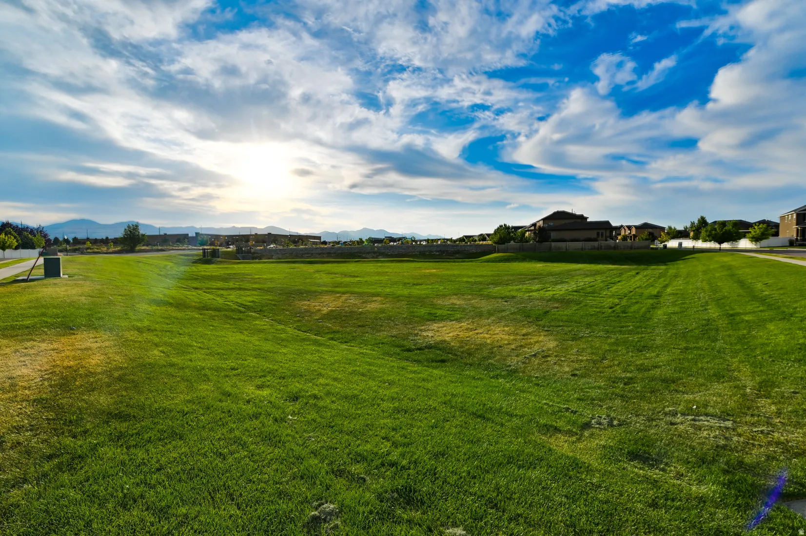 Expansive green space featuring a large lawn area, distant mountain backdrop, and surrounding residential structures