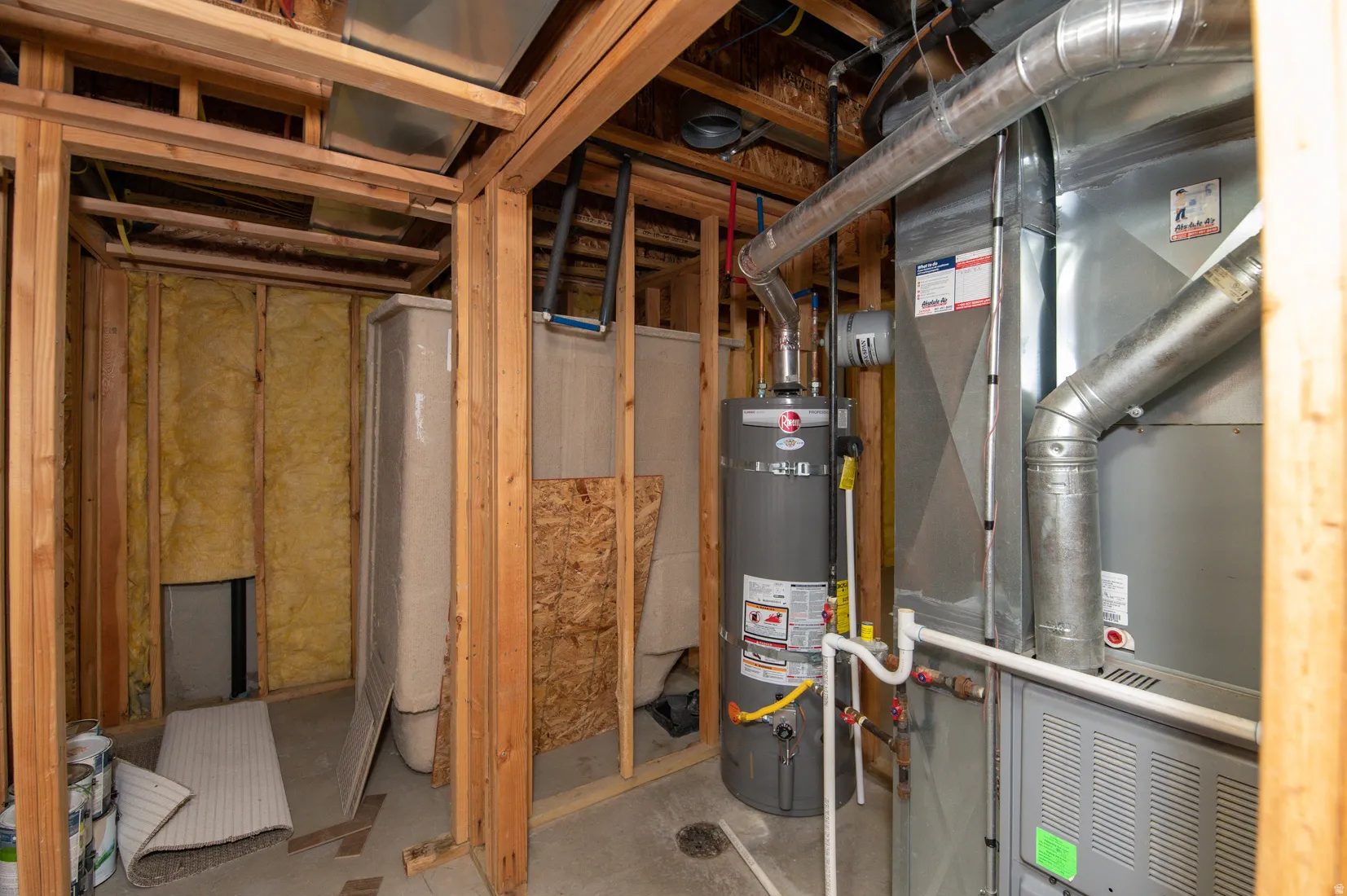 Basement utility area featuring exposed wood framing, a water heater, a furnace, and ductwork