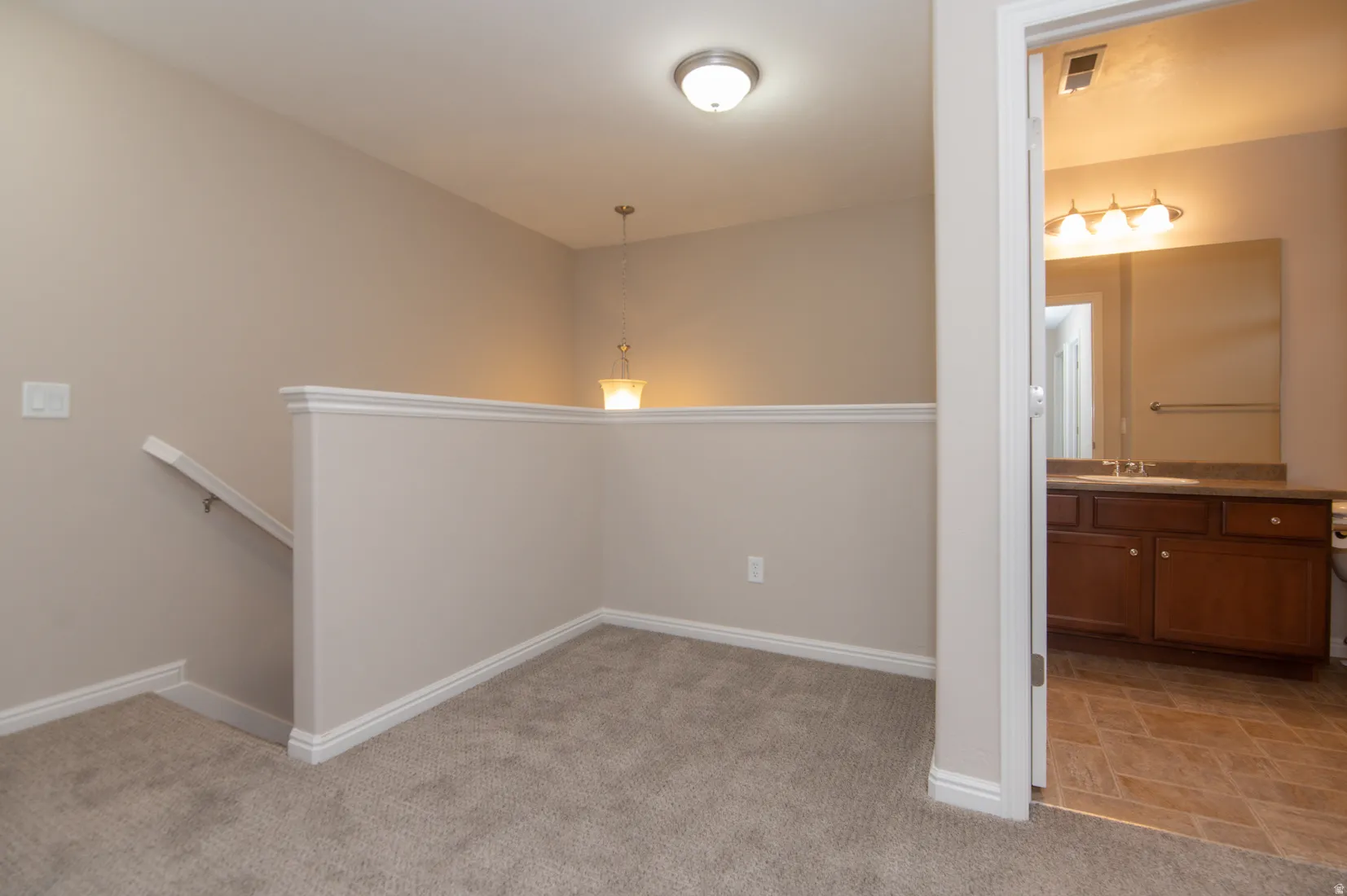 Carpeted landing area featuring a painted railing with white trim, a semi-flush mount ceiling fixture, and a decorative pendant light