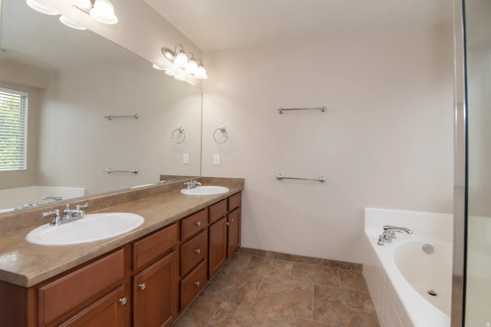 Bathroom featuring a double vanity with ample storage cabinetry, a large built-in mirror, an integrated soaking tub, and tiled flooring
