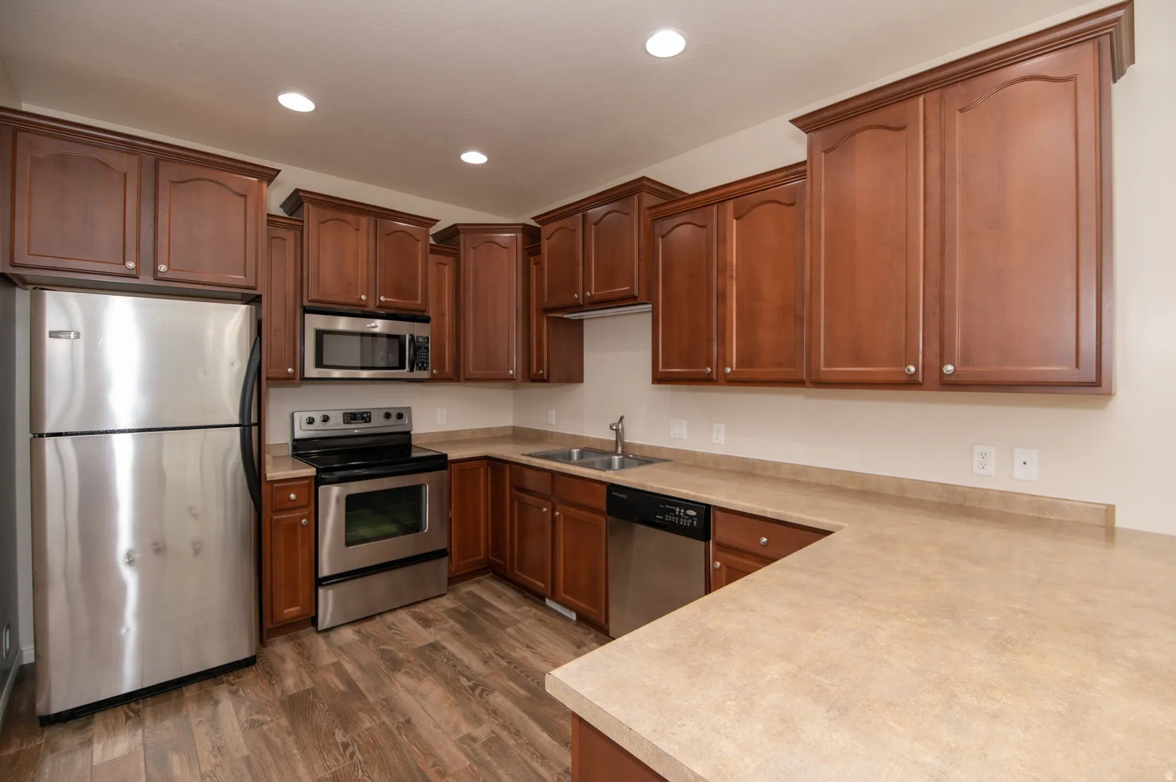 U-shaped kitchen featuring wood-finish cabinetry, stainless steel appliances, neutral countertops, and wood-finish flooring