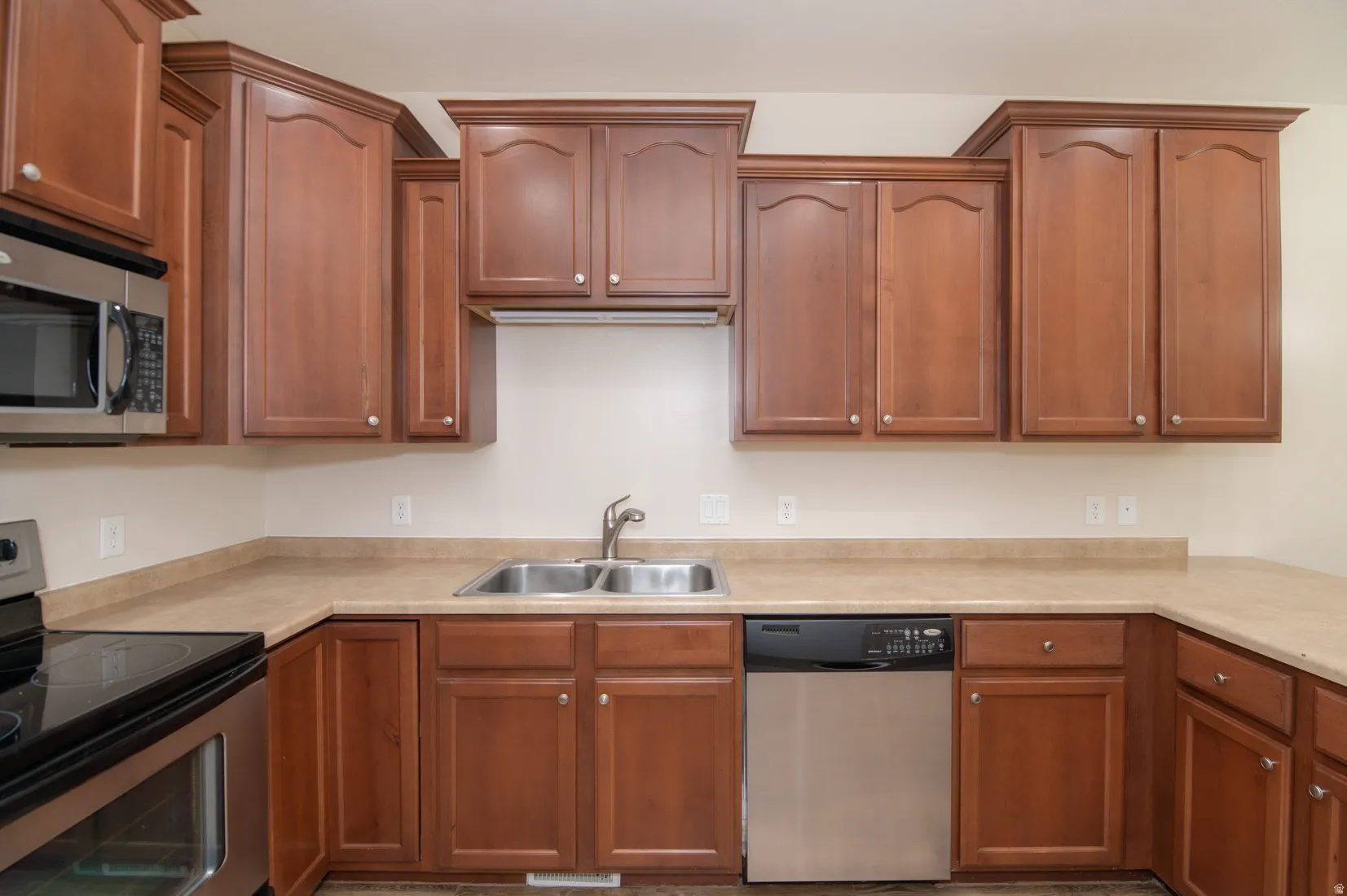 Kitchen featuring wood-finish cabinetry with crown molding, stainless steel appliances, and a dual basin sink