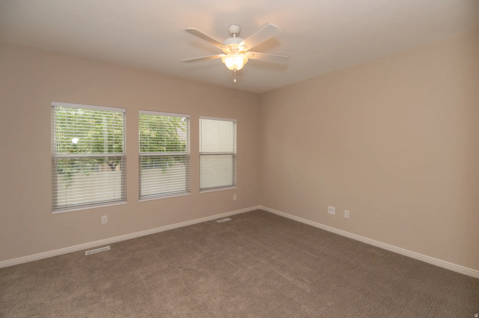 Room featuring three windows with horizontal blinds, neutral wall paint, and plush carpet flooring
