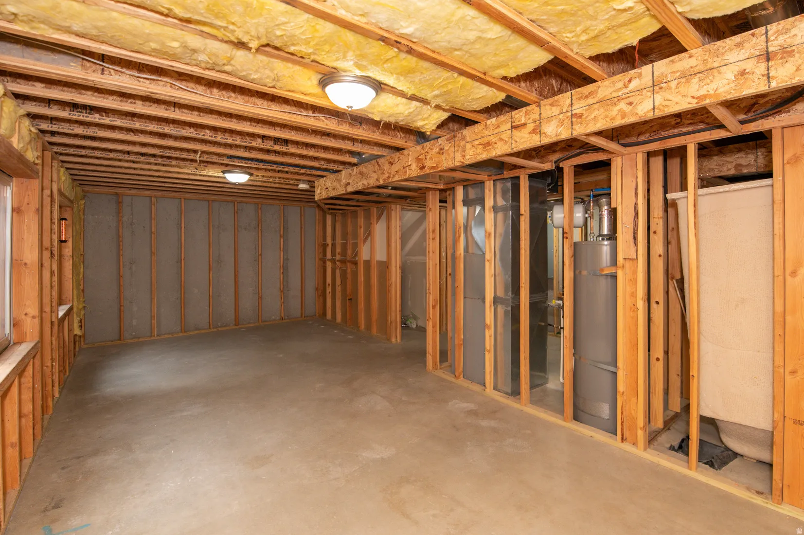 Unfinished basement featuring exposed wood framing, concrete flooring, visible insulation in the ceiling, and flush-mount ceiling lighting