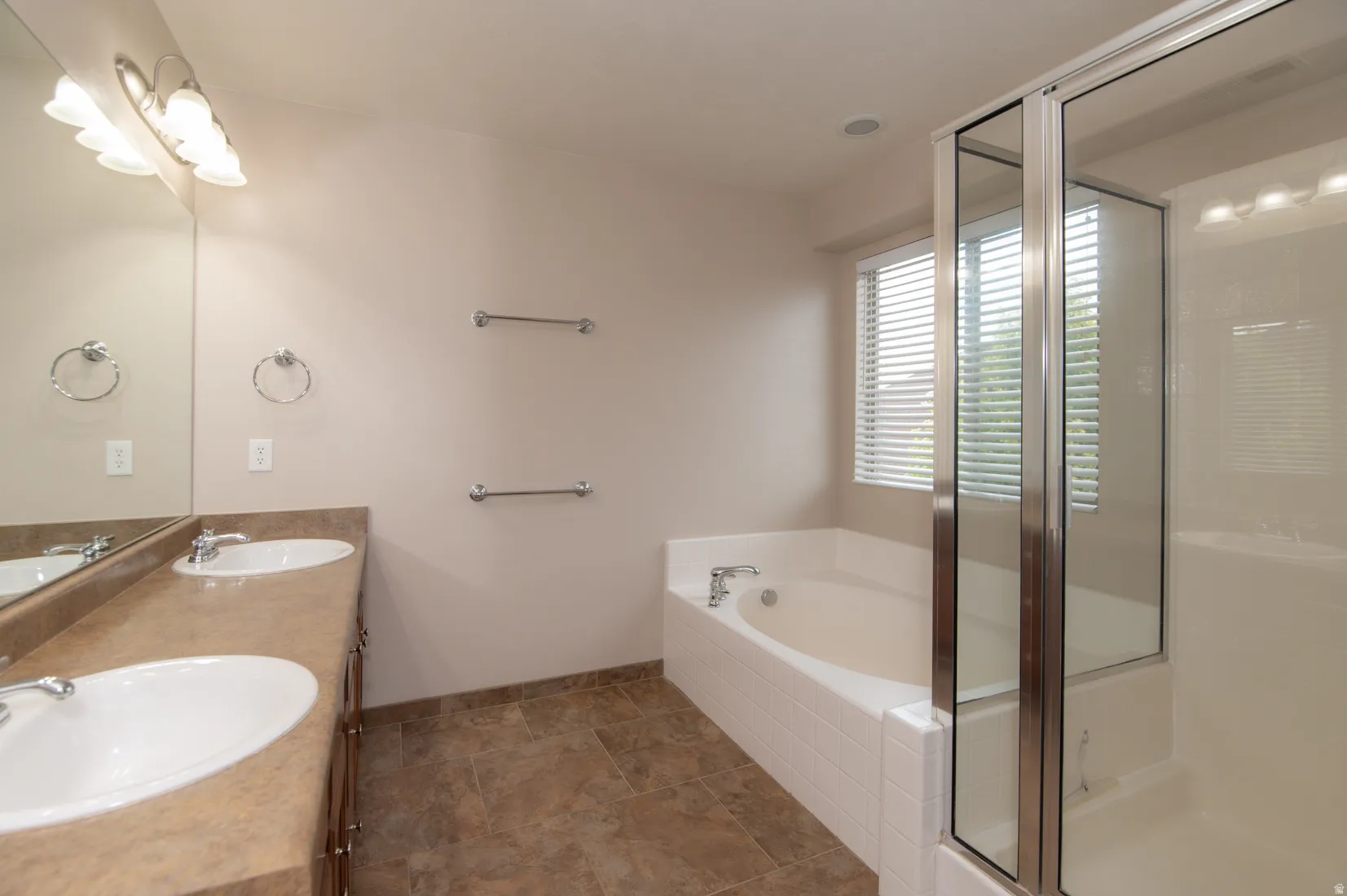 Bathroom featuring a dual vanity with undermount sinks, a built-in bathtub, a glass-enclosed shower, and tile flooring