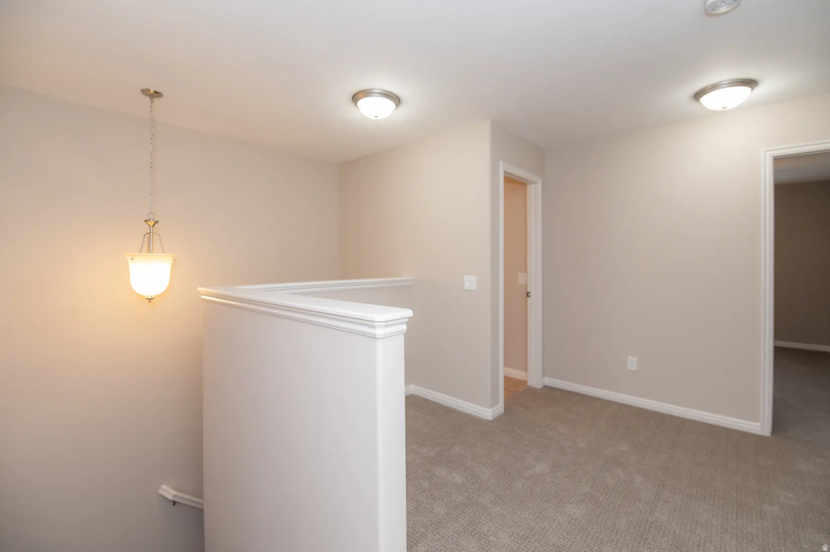 Upper-level hallway featuring neutral wall paint, carpet flooring, a white banister, and a hanging pendant light with an opaque glass shade