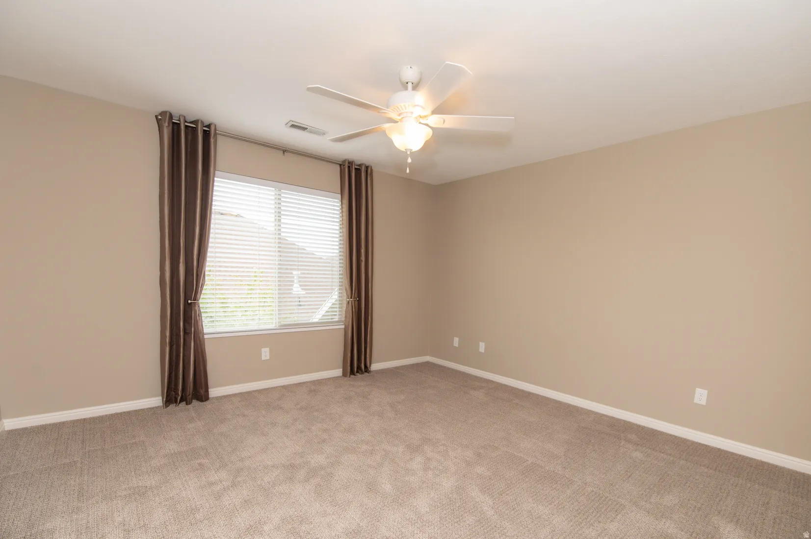 Spacious room featuring neutral wall paint, light-toned carpeting, a window with horizontal blinds, and a ceiling fan with integrated lighting