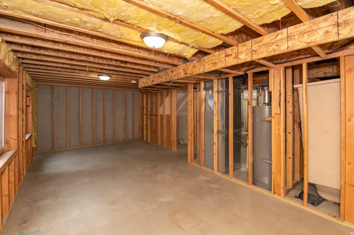 Unfinished basement featuring exposed wood framing, concrete flooring, visible insulation in the ceiling, and flush-mount ceiling lighting