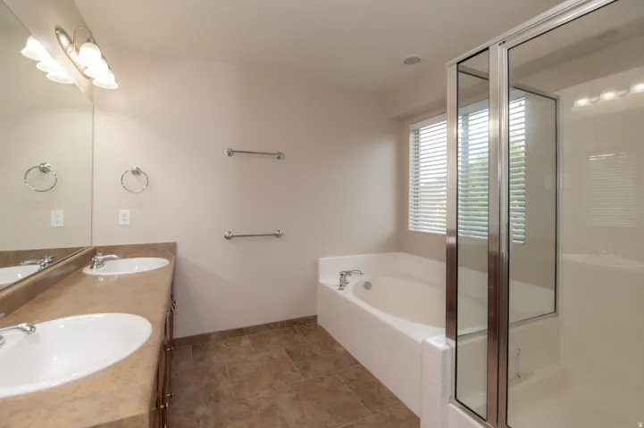 Bathroom featuring a dual vanity with undermount sinks, a built-in bathtub, a glass-enclosed shower, and tile flooring